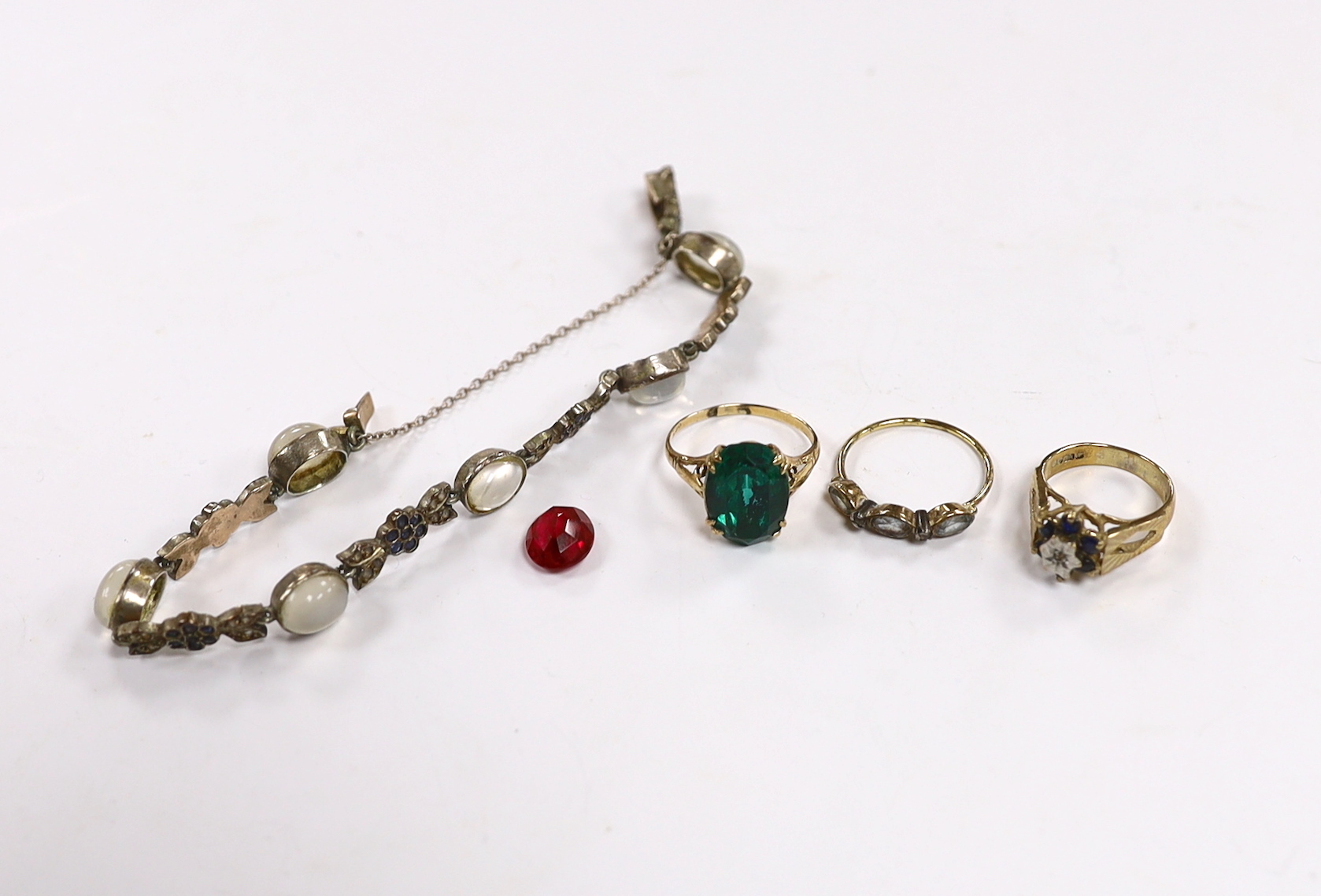 Two 9ct and gem set rings, one other costume ring, an unmounted oval cut synthetic ruby and a moonstone and paste set white metal bracelet.